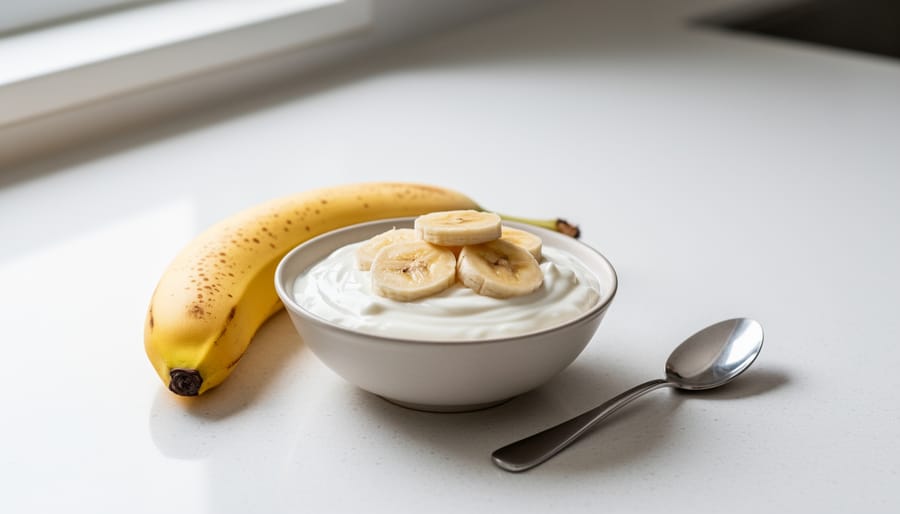 Two medium bananas on a white plate next to plain Greek yogurt, photographed in bright natural light.