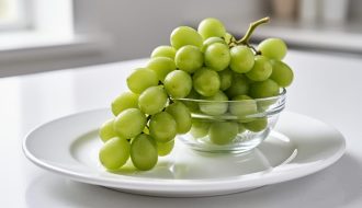 Close-up of fresh seedless green grapes with visible water droplets, arranged on a white plate beside a glass bowl.